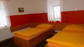 Una habitación con dos camas individuales, cortinas blancas, una pared roja y un cuadro pequeño en la pared.