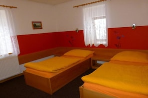 A room with two single beds, white curtains, a red wall, and a small picture on the wall.