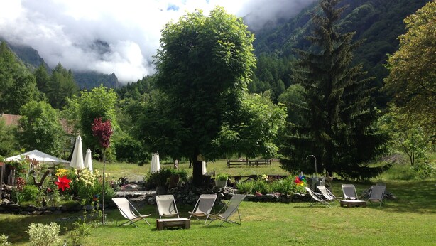 A serene outdoor seating area with lounge chairs and umbrellas, surrounded by lush greenery and a mountainous backdrop. - Auberge Gaillard (La Motte-en-Champsaur)
