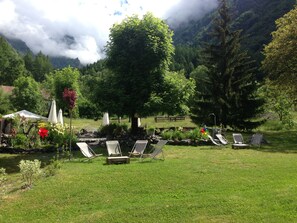 A serene outdoor seating area with lounge chairs and umbrellas, surrounded by lush greenery and a mountainous backdrop. - Auberge Gaillard (La Motte-en-Champsaur)