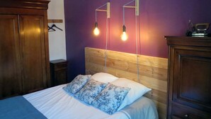 A bedroom with a wooden headboard, a bed with white bedding and blue floral pillows, and two wall-mounted light fixtures. - Auberge Gaillard (La Motte-en-Champsaur)