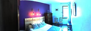 A bedroom with a wooden headboard, a bed with blue floral pillows, a nightstand, a dresser, two chairs, and a mirror on the wall. - Auberge Gaillard (La Motte-en-Champsaur)