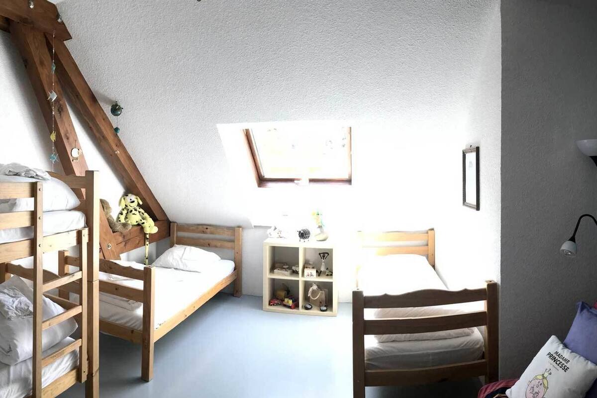 Ein Zimmer mit Etagenbetten, einem Bücherregal, einer farbenfrohen Wand mit gerahmten Bildern und einer Lampe.