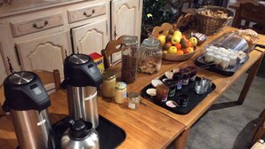 A wooden table with a variety of food items and condiments, including jars, a thermos, and a basket of fruits. - Auberge Gaillard (La Motte-en-Champsaur)
