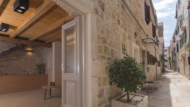 A narrow stone corridor with a wooden door leading to a room with a modern kitchen. - Casa Sepia (Trogir)
