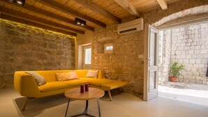 A room with a yellow sofa, a round table, and a stone wall. - Casa Sepia (Trogir)