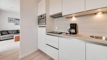 A modern kitchen with white cabinets, a built-in oven, a coffee maker, and a lighted backsplash.