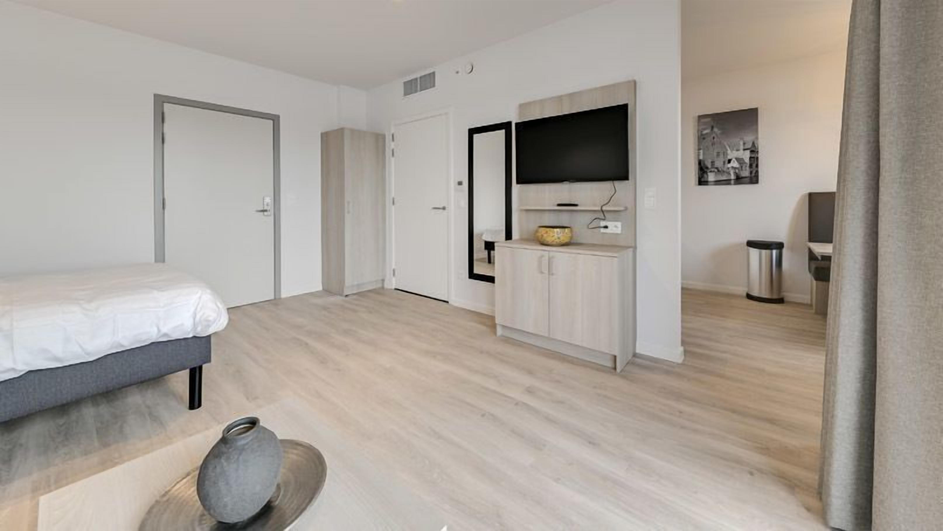 Une chambre d’hôtel moderne équipée d’un lit, d’une petite armoire, d’une télévision et d’une poubelle.