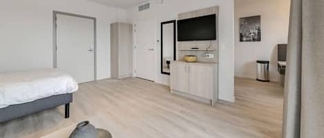 Une chambre d’hôtel moderne équipée d’un lit, d’une petite armoire, d’une télévision et d’une poubelle.