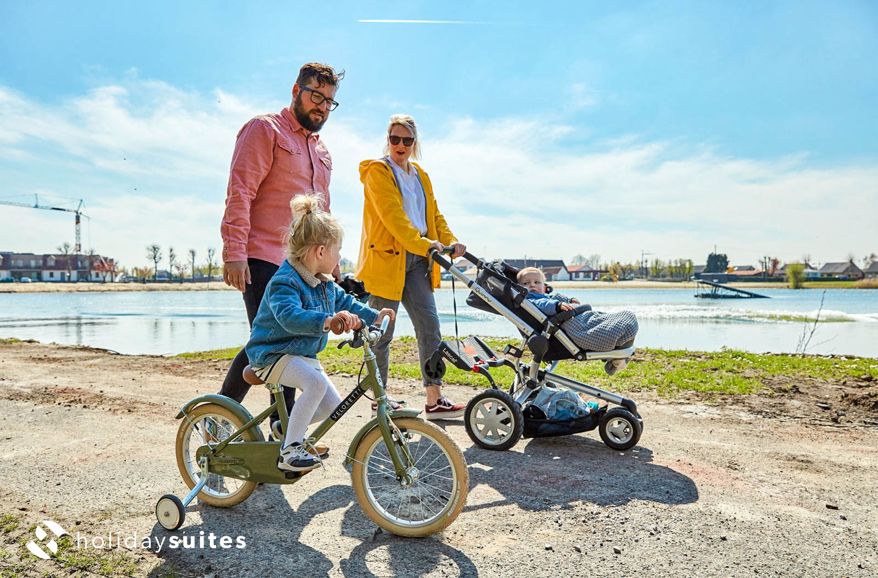A family by a lake with a child on a tricycle and a stroller.