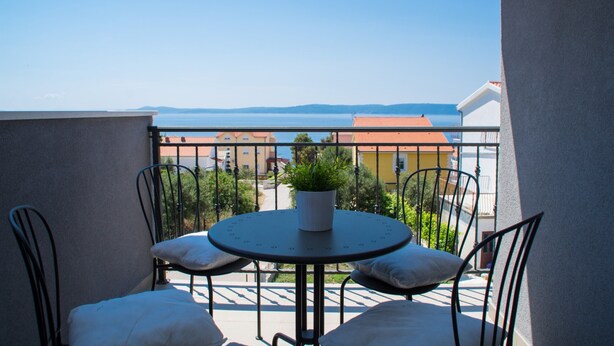 A balcony with a round table and chairs, a potted plant, and a view of buildings and water. - Apartment Flynn (Okrug)