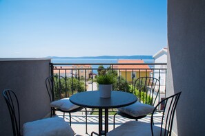 Un balcone con un tavolino rotondo e sedie, un vaso con una pianta e vista su edifici e acqua.