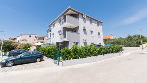 A multi-story residential building with balconies, a paved driveway, and a green hedge in front. - Apartment Flynn (Okrug)