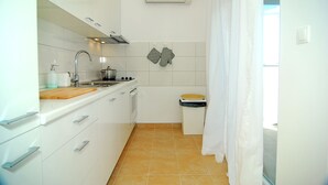 A compact kitchen with white cabinets, a wooden countertop, a sink, and a stove. - Apartment Flynn (Okrug)
