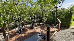 Un gimnasio al aire libre con equipo de ejercicio, rodeado de árboles y una terraza de madera.