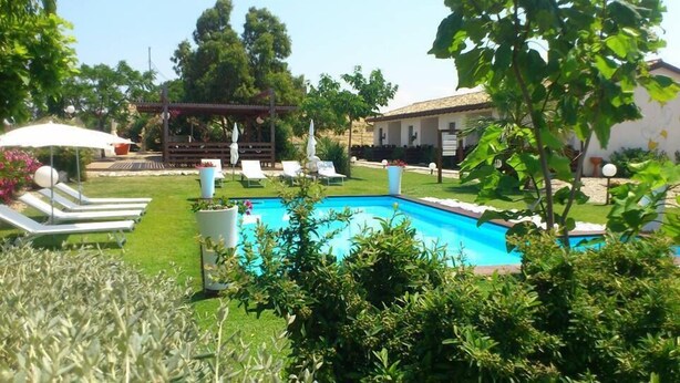 Una piscina rodeada por un césped cuidado con sillas de descanso y una pérgola.