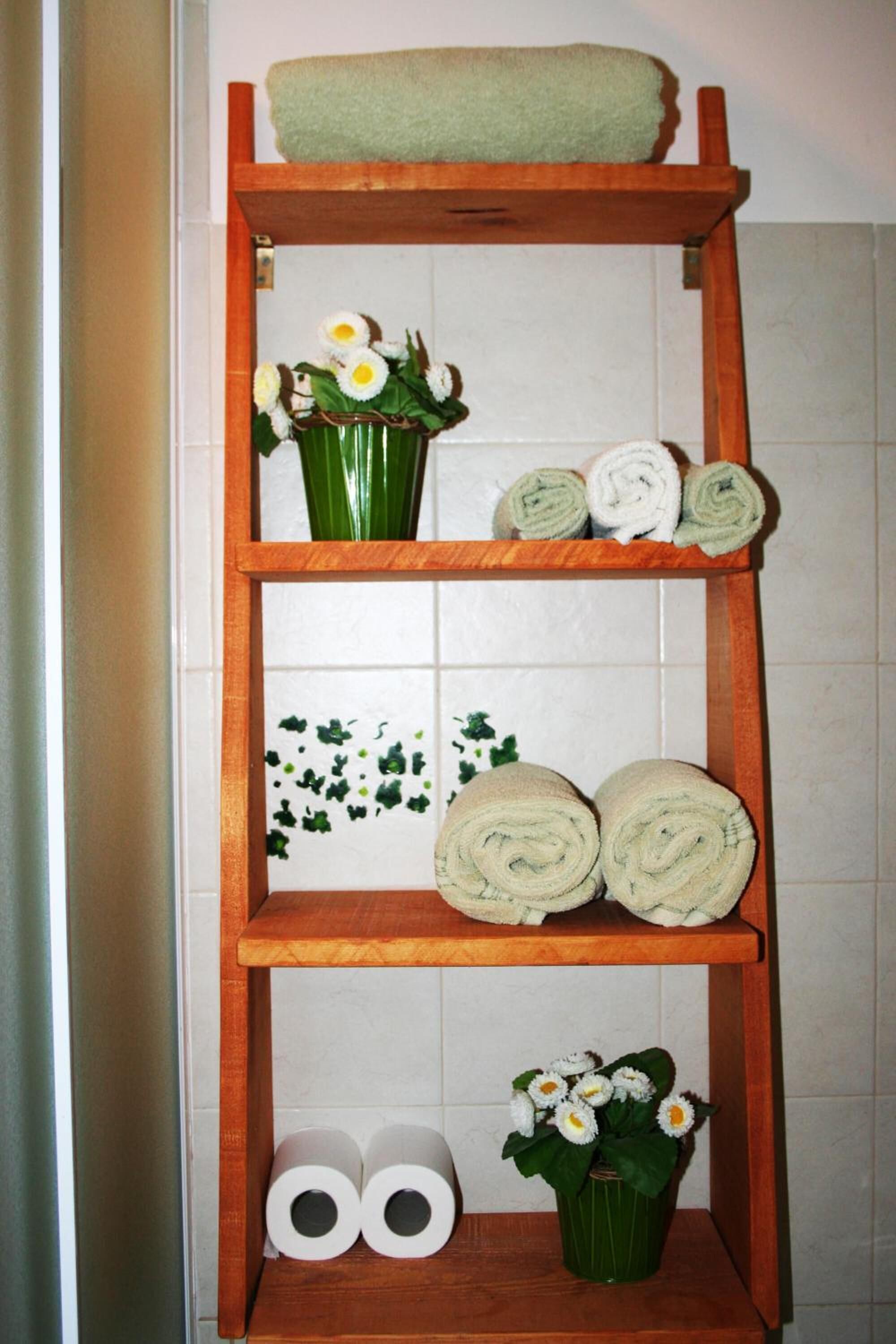 A wooden shelf with towels, a vase with flowers, and toilet paper.