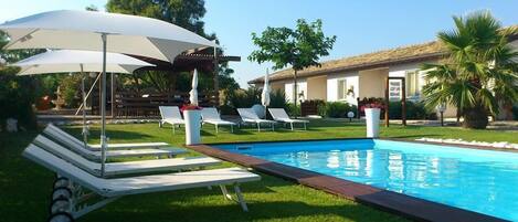 A swimming pool with lounge chairs and umbrellas, surrounded by a well-maintained lawn and a house in the background.
