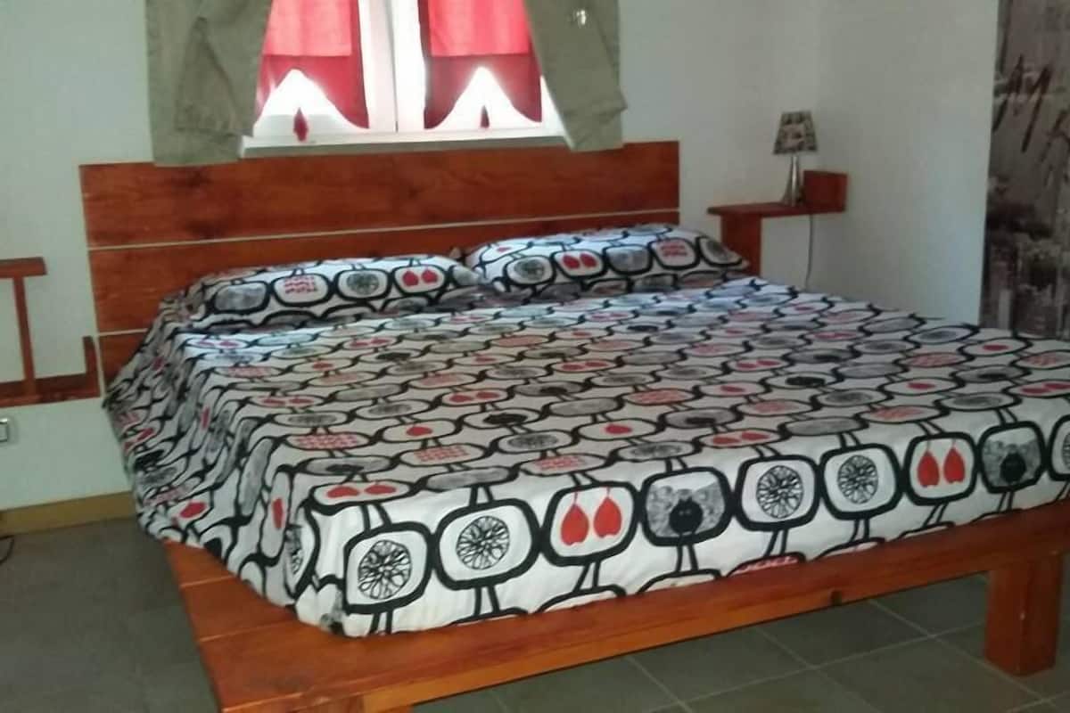 Une chambre à coucher avec un cadre de lit en bois, une literie à motifs, une fenêtre avec des rideaux rouges et une table de chevet avec une lampe.