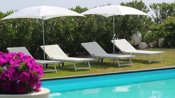 Un espace aménagé au bord de la piscine, avec des chaises longues blanches et des parasols, le tout entouré de verdure.