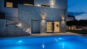 Un edificio moderno con facciata in pietra, piscina e ingresso carrabile.