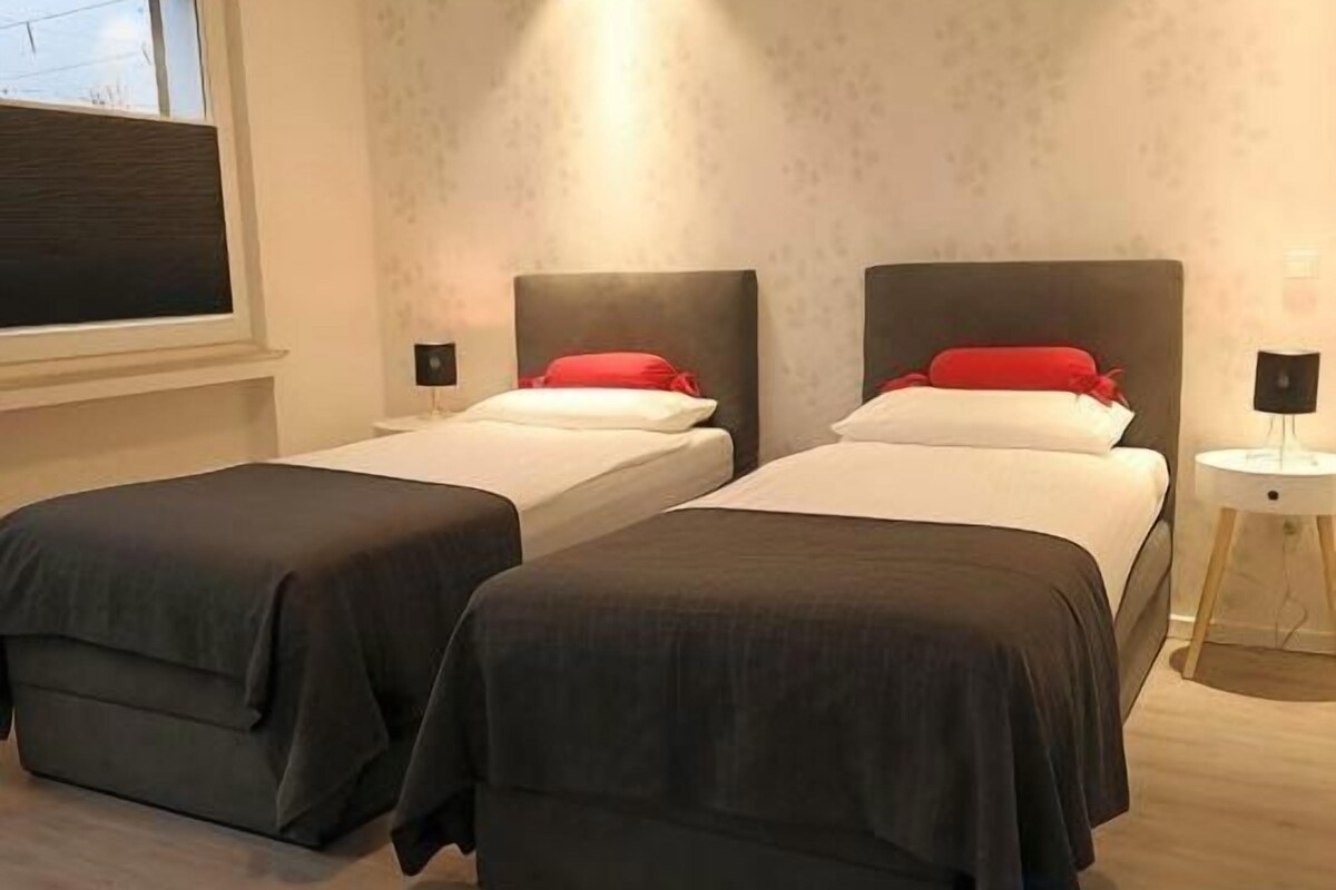 A hotel room with two beds, a bedside table, and a window.