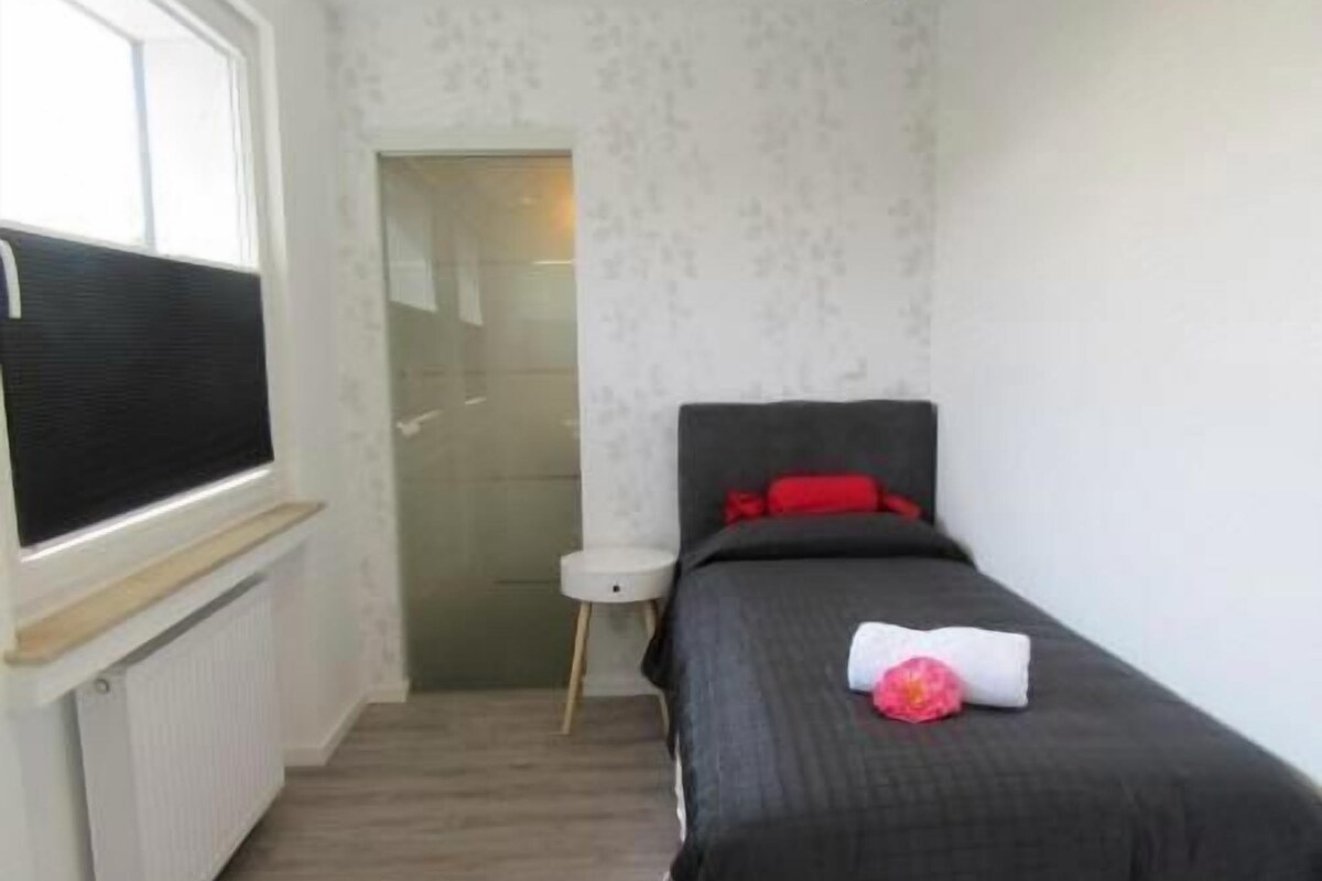 A small, narrow room with a single bed, a window, and a radiator.