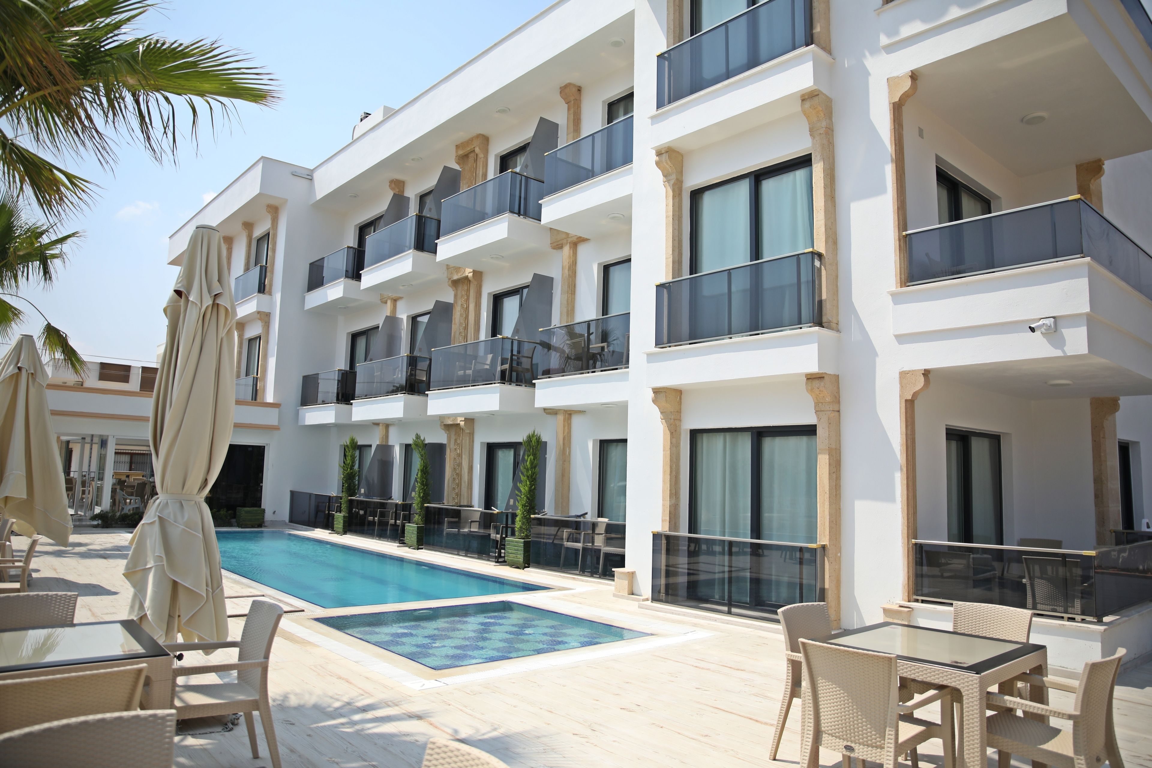 A modern hotel with a swimming pool, outdoor seating, and multiple balconies.