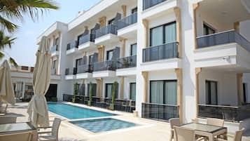 A modern hotel with a swimming pool, outdoor seating, and multiple balconies.