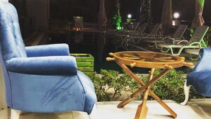 A poolside area with two blue lounge chairs, a wooden table, and a pool with a green-lit edge. - Kaptan Suit Otel (Silifke)