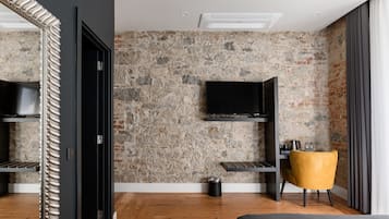 A modern hotel room with a stone wall, a flat-screen TV, a wooden floor, a bed, a yellow chair, and a black door.