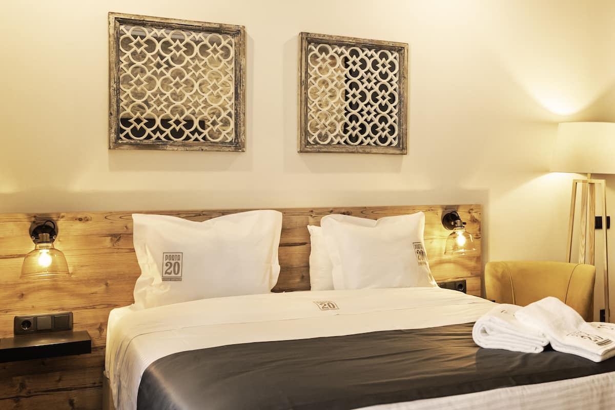 Une chambre d’hôtel avec une tête de lit en bois, deux tables de chevet avec des lampes, un lit avec une literie blanche et des panneaux décoratifs sur les murs.