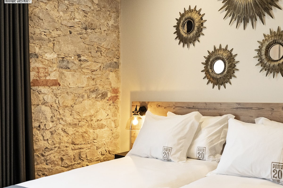 Une chambre d’hôtel avec un mur en pierre, une tête de lit en bois et quatre miroirs décoratifs en forme de soleil accrochés au mur.