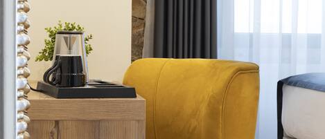 Una habitación moderna con una mesita de madera, un sillón amarillo, una cama y una cafetera.