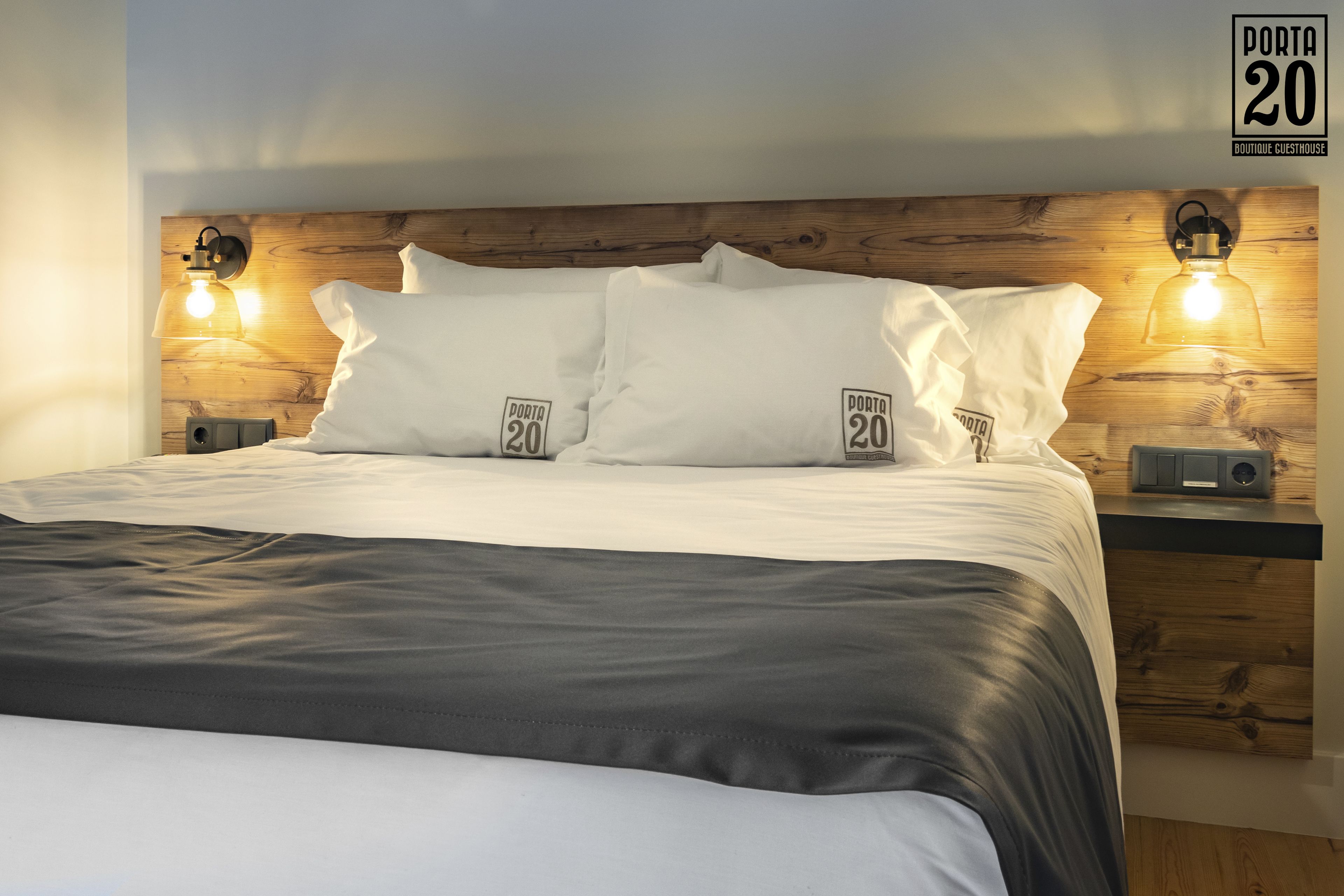 A neatly made bed with white linens and a black throw, flanked by wooden headboards with built-in lighting.