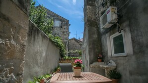 Une petite cour étroite, avec une table et des chaises en bois, entourée de murs en pierre et agrémentée de plantes en pot.