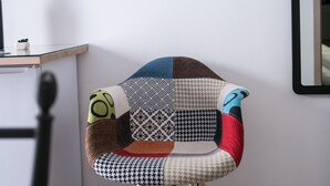 Une chaise dotée d’un siège en patchwork et de pieds en bois, placée dans une pièce où un téléviseur à écran plat est fixé au mur.