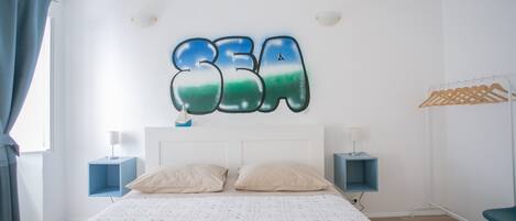 A bedroom with a bed, two bedside tables, a wall-mounted artwork, a wardrobe, and a hanging clothes rack.