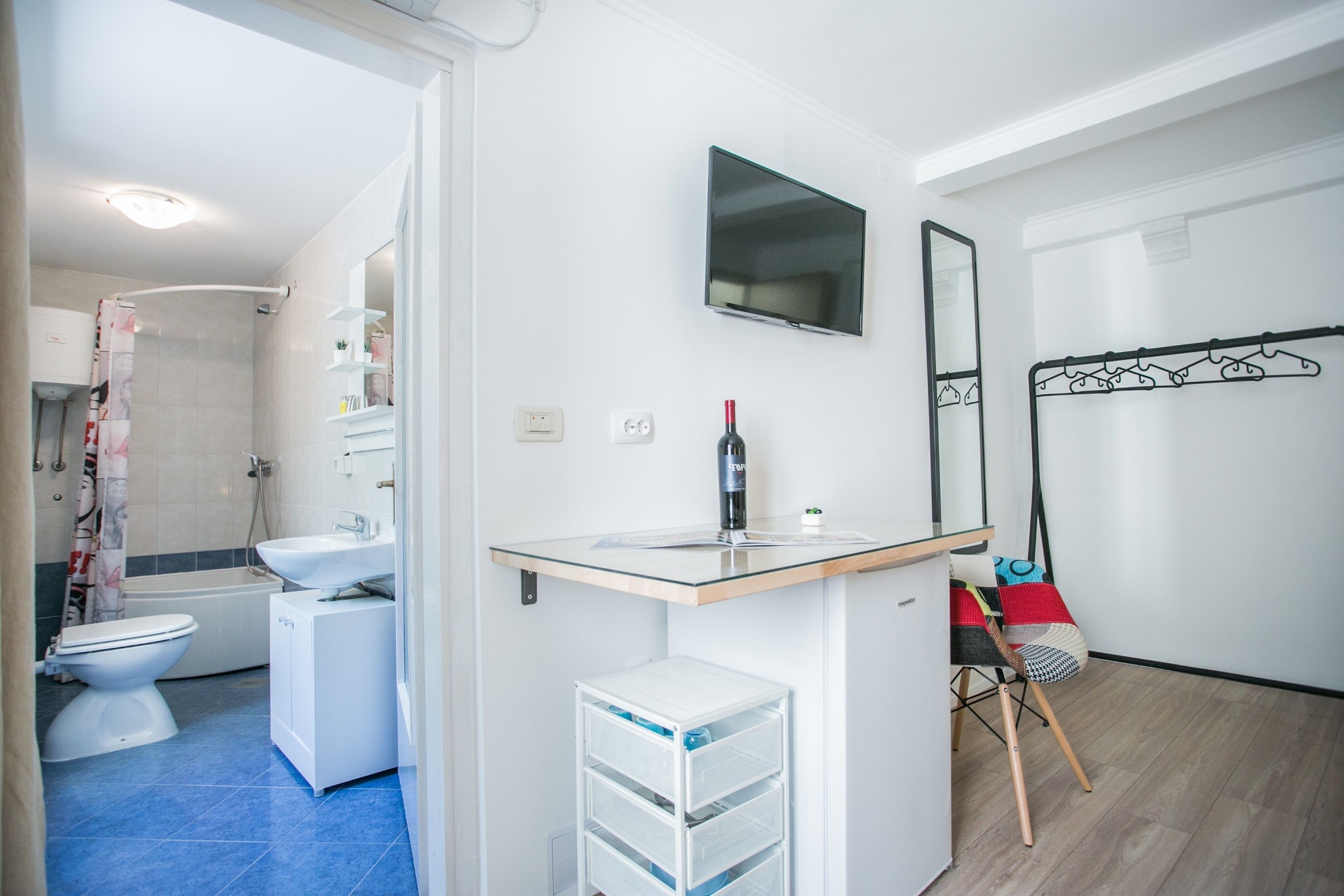 Un bagno moderno con doccia, toilette e lavandino. C'è una TV a parete e una bottiglia di vino sul ripiano.