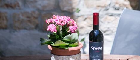 A bottle of wine and a potted plant on a wooden table against a stone wall.