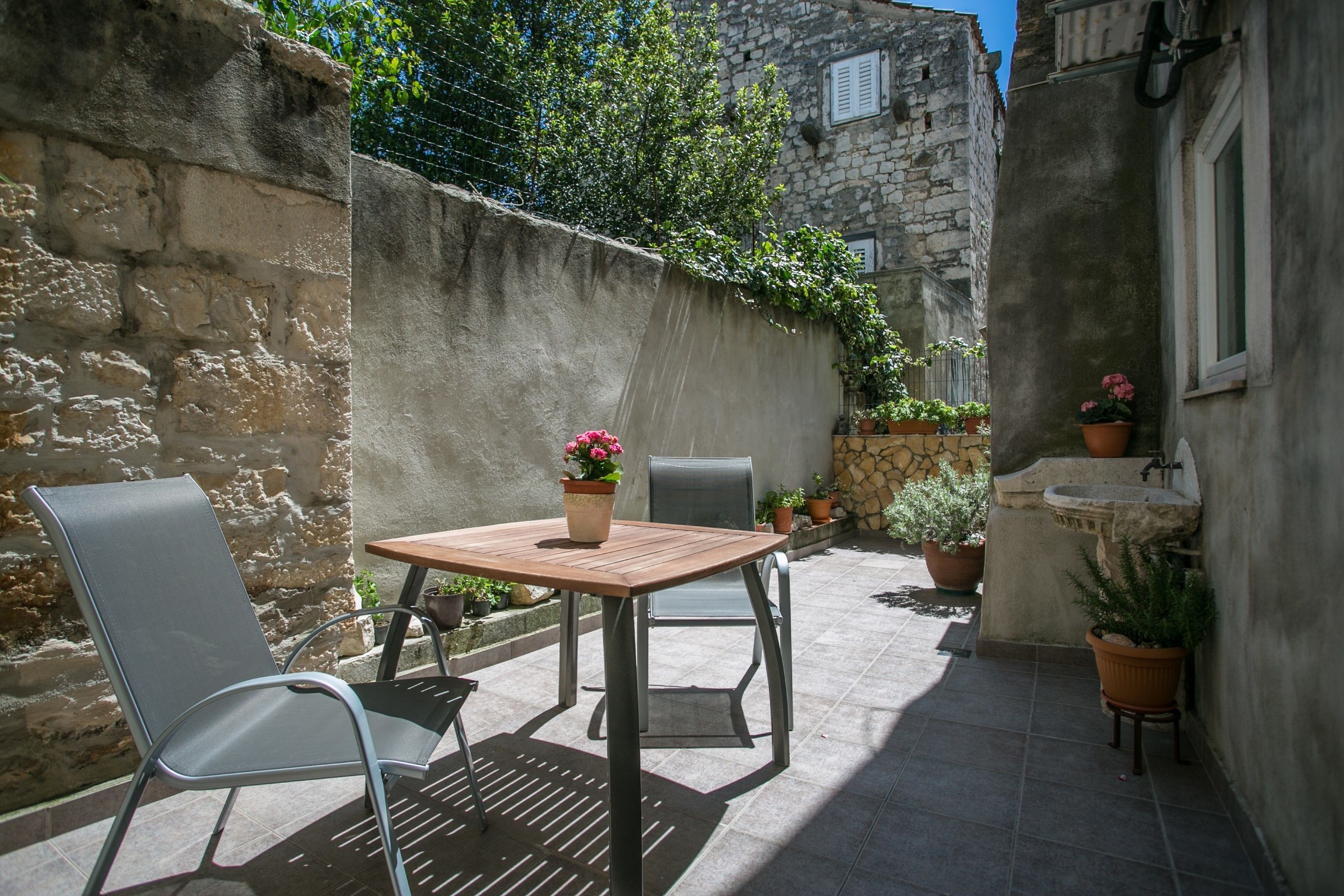 Een terras met twee stoelen en een tafel, omgeven door stenen muren en plantenpotten.