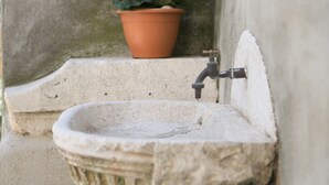 Un évier en pierre avec un robinet, une plante en pot aux fleurs roses et une fenêtre.