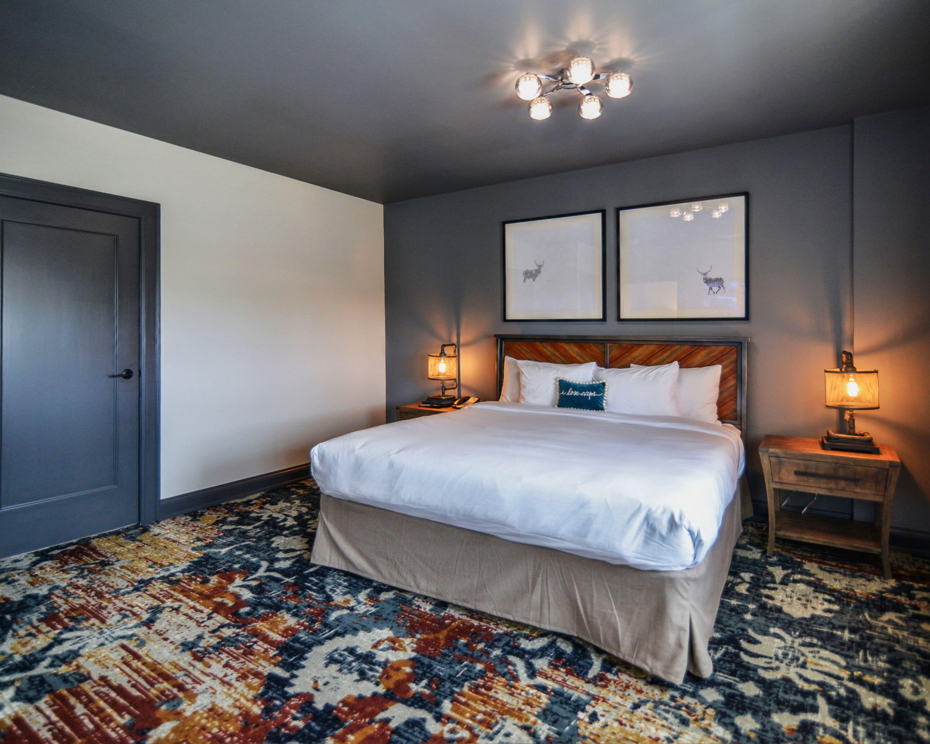 Une chambre d’hôtel avec un grand lit, deux tables de chevet, une moquette à motifs et un luminaire au plafond.
