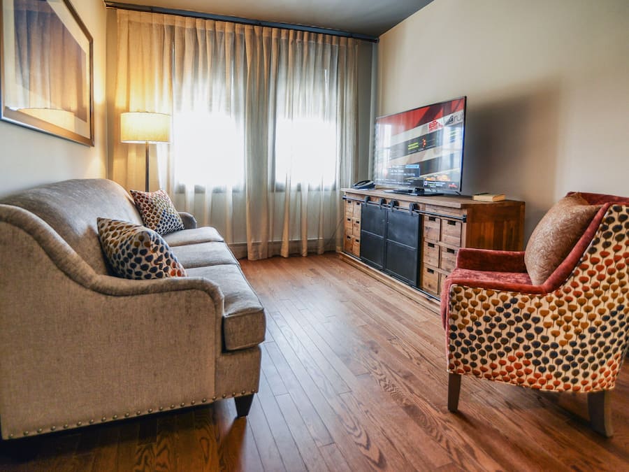 Un salon comprenant un canapé, un fauteuil à motifs, un téléviseur et un meuble en bois.