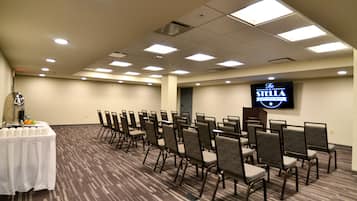 A conference room with rows of chairs, a table with a white tablecloth, and a sign for "The Stella Hotel & Ballroom".