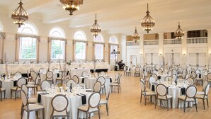 A large banquet hall with multiple round tables and chairs, ornate chandeliers, and large windows. - The Stella Hotel & Ballroom (Kenosha)