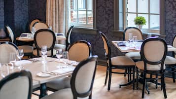 Comedor con mesas dispuestas para cuatro personas, sillas y ventana con vista a edificios.