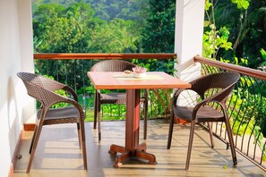Varanda com cadeiras de vime e uma mesa, com vista para uma paisagem verdejante.