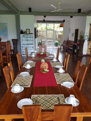 Uma sala de jantar com uma mesa de madeira comprida posta para refeição, cercada por cadeiras.