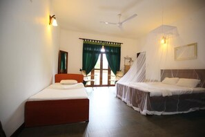 Quarto com duas camas, uma delas com dossel, ventilador de teto e vista para o exterior através de uma porta com cortinas verdes.